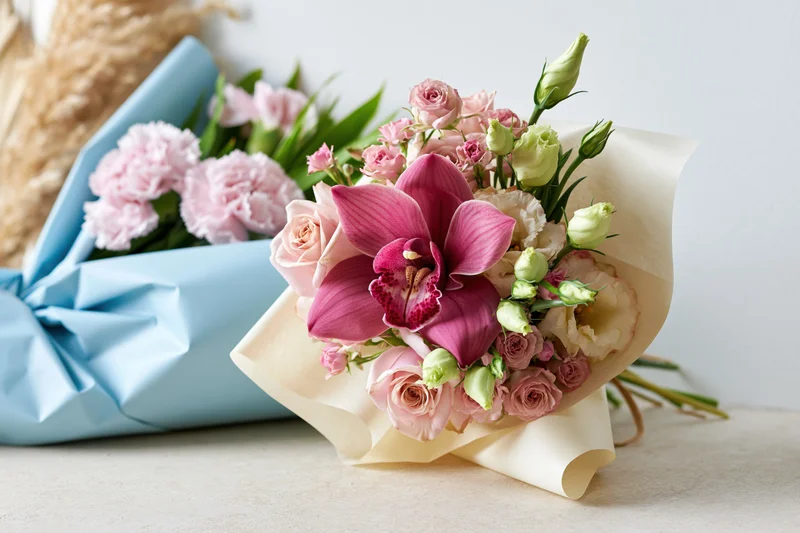 Two wrapped bouquets of pink roses, orchids and carnations arranged side by side on a light surface