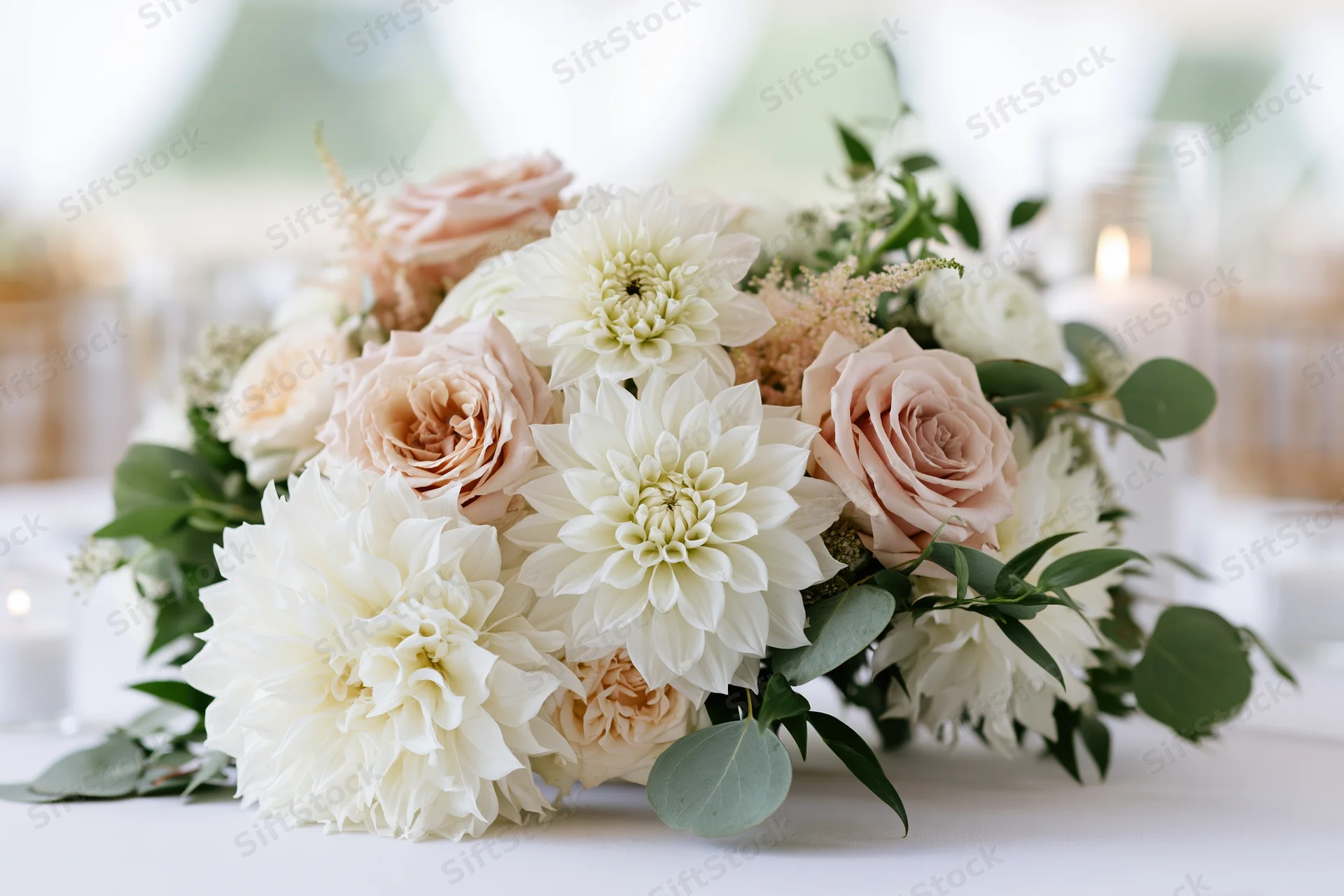 Wedding centerpiece of white dahlias and blush garden roses on a table with greenery and candles