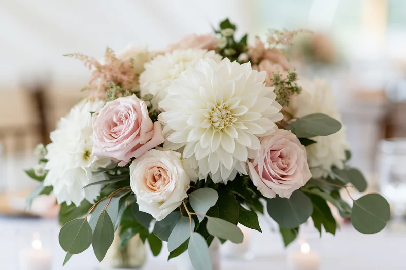 Wedding centerpiece of white dahlias and blush garden roses on a table with candles