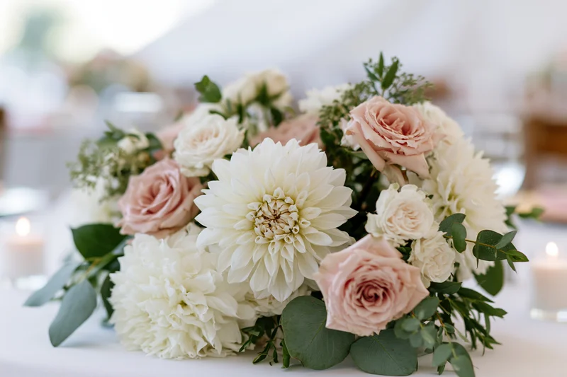 White dahlias and blush garden roses arranged as a wedding centerpiece on a table with candles