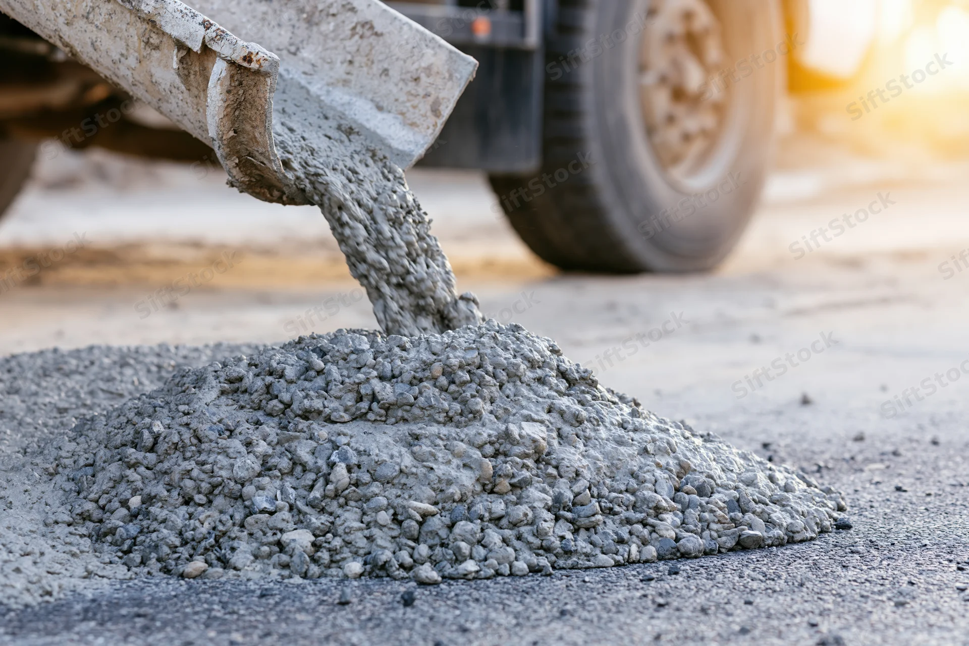 Wet concrete pouring from a cement mixer chute onto a road surface