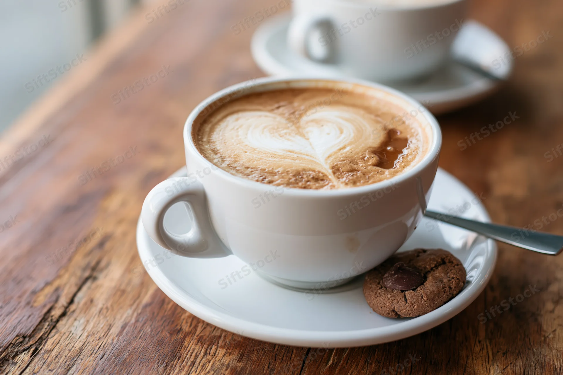 Cappuccino with heart-shaped latte art and chocolate chip cookie on a wooden table