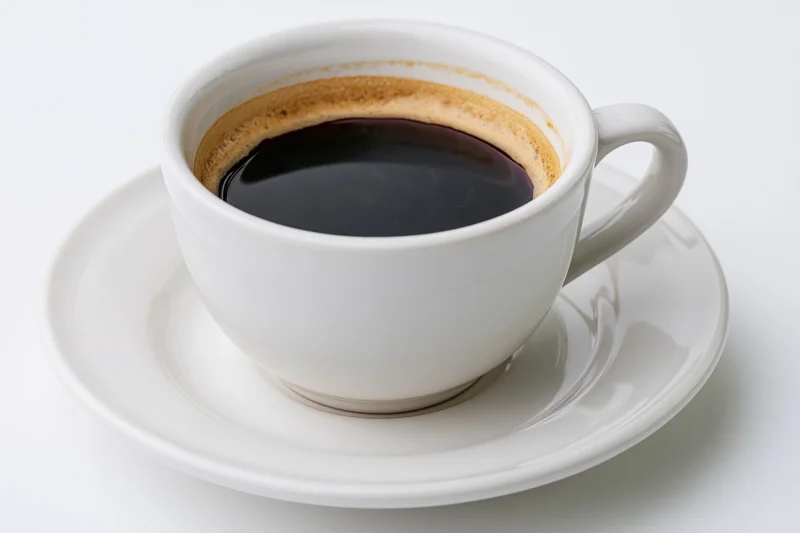 White ceramic coffee cup filled with black coffee on a matching saucer against a plain white background