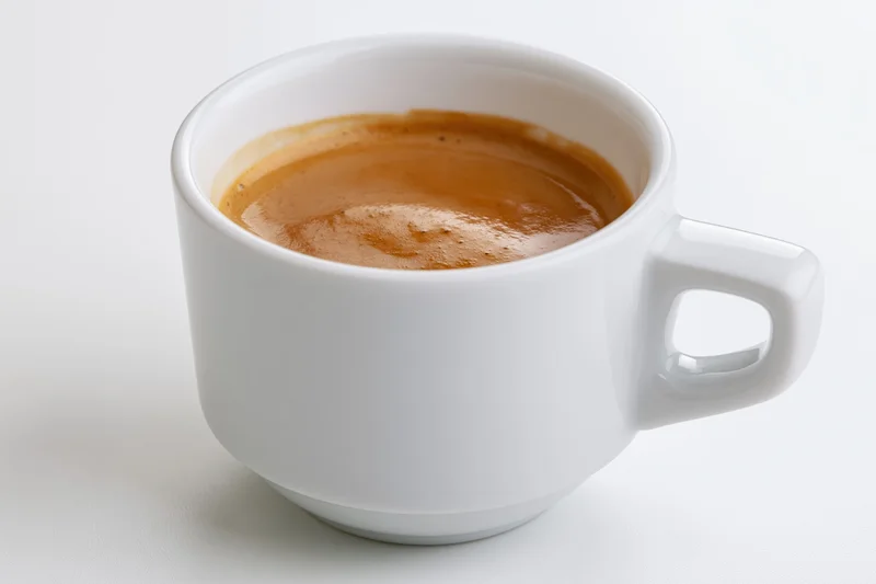 White ceramic cup filled with espresso showing thin crema on plain surface