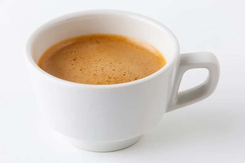 White ceramic cup filled with espresso showing crema on plain white surface