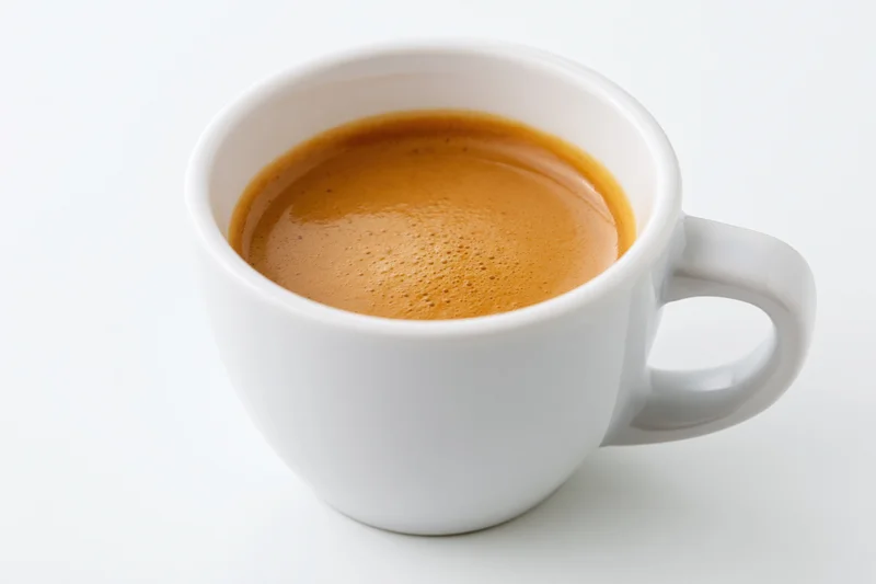 White ceramic cup filled with espresso showing crema on plain white surface