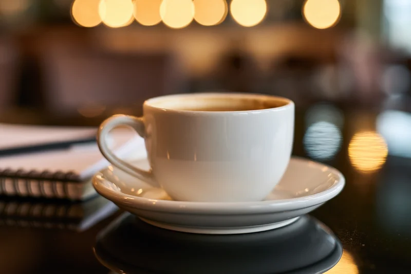 White ceramic coffee cup on saucer resting on dark reflective table in cafe interior