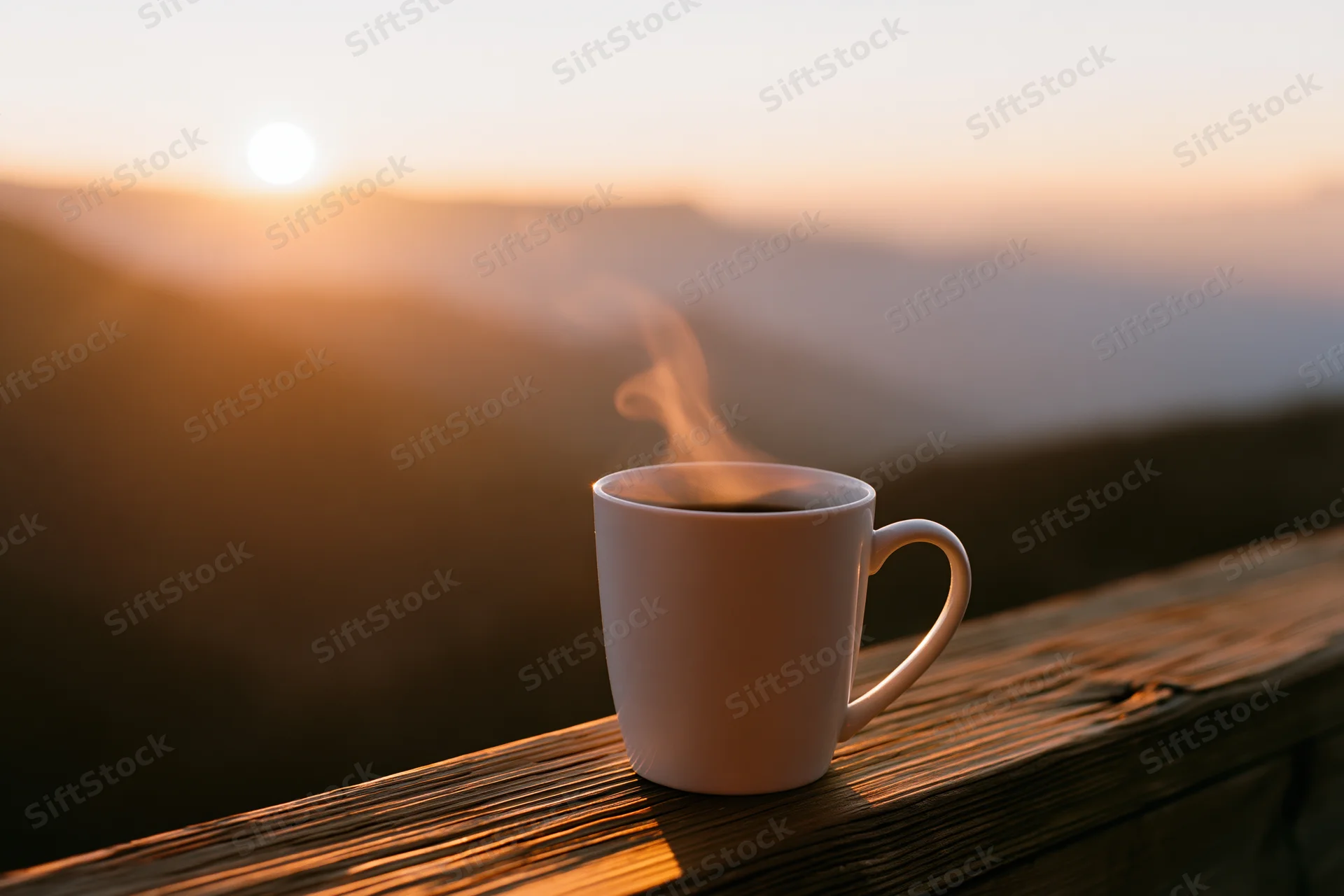 White ceramic coffee mug with steam on wooden railing overlooking mountain sunrise
