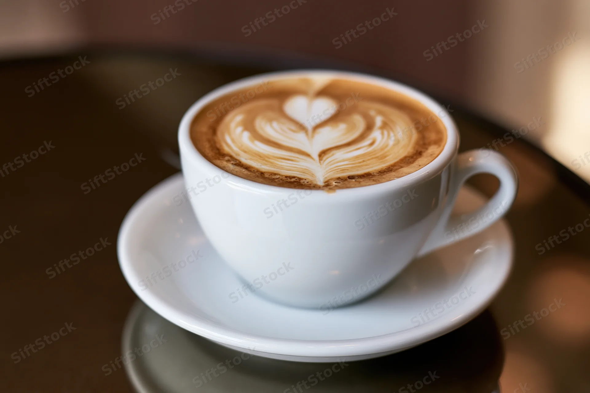 White ceramic cup of latte art coffee with heart and leaf pattern on saucer on wooden table