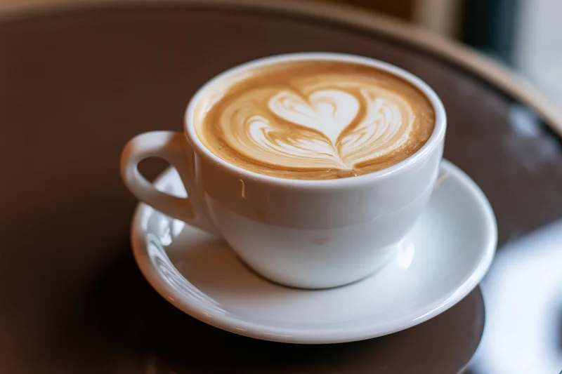 White ceramic cup of latte art coffee with heart and leaf design on saucer on brown table