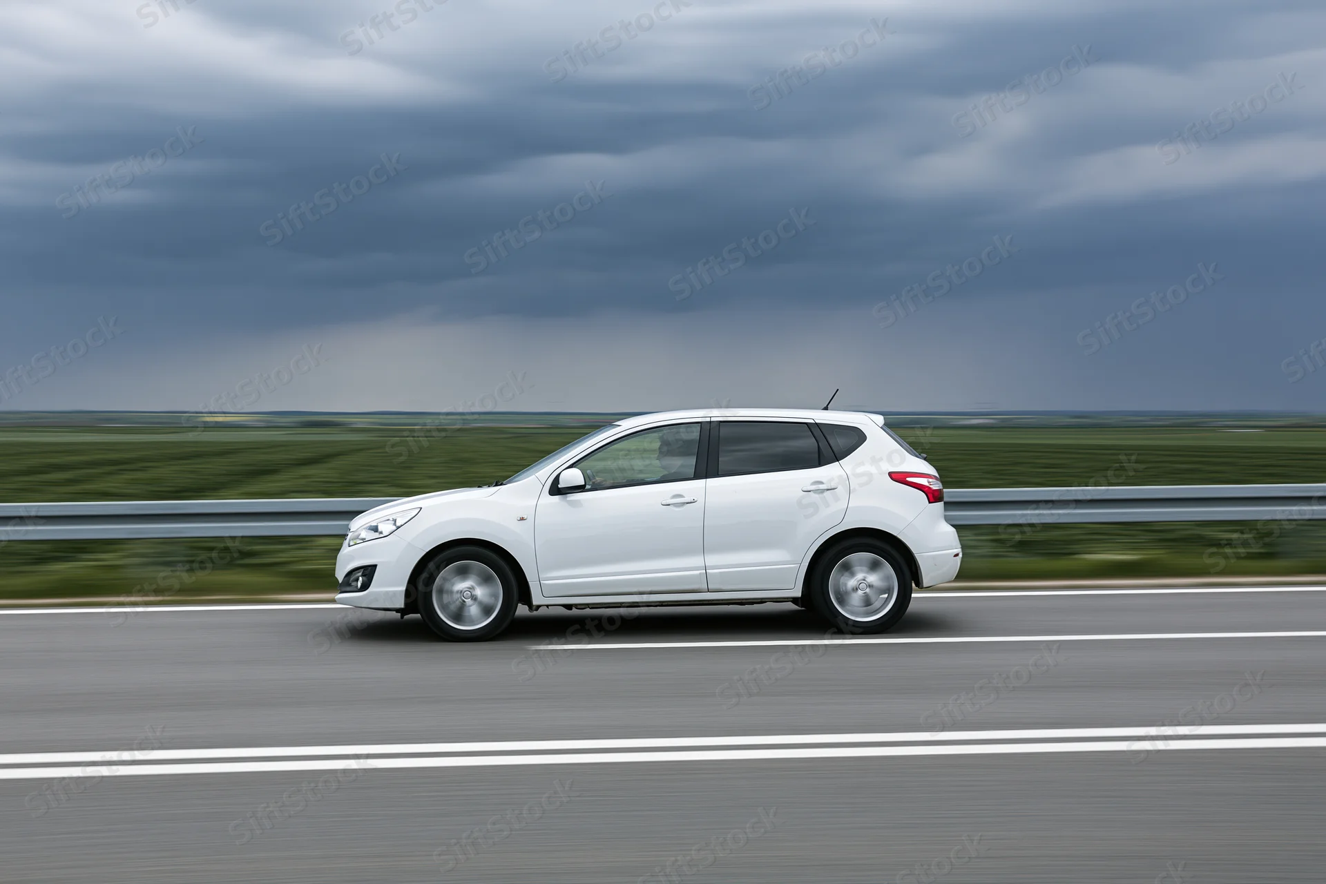 White compact suv driving on highway with blurred rural landscape and overcast sky