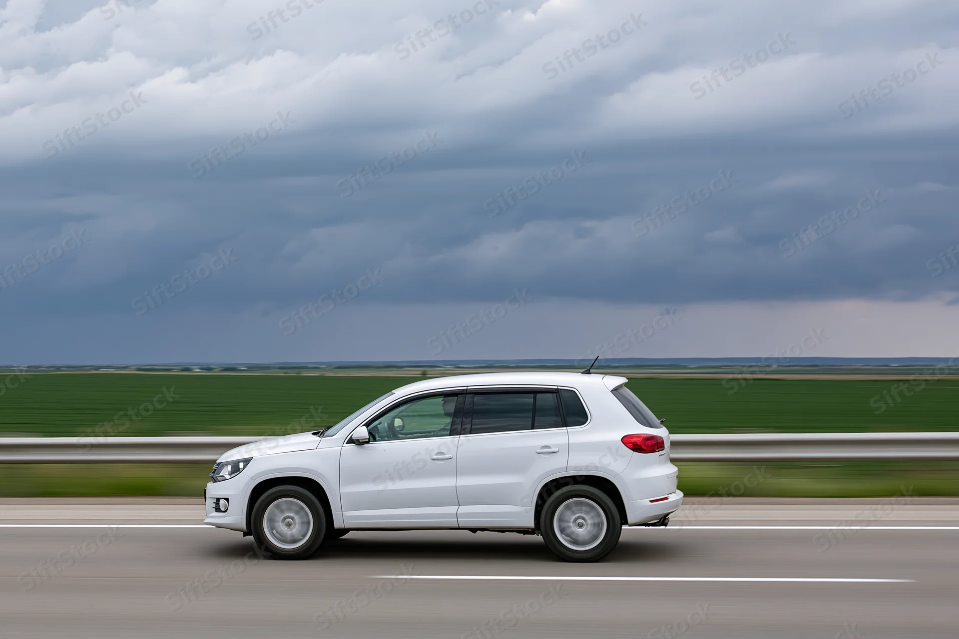 White compact suv driving on highway with blurred rural landscape and cloudy sky
