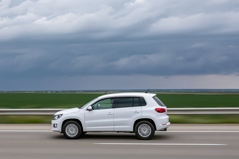 White compact suv driving on highway with blurred rural landscape and cloudy sky