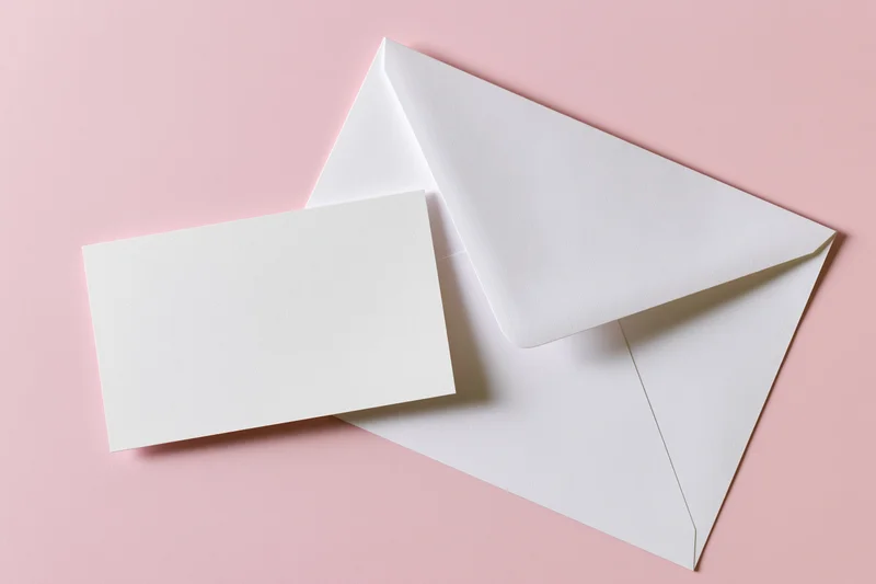 White envelope with triangular flap and blank card on pink background