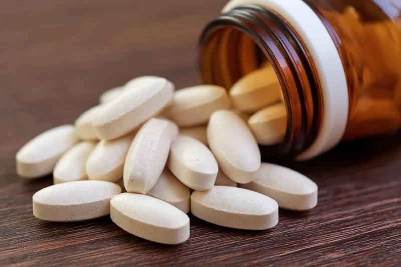 White oval supplement tablets spilling from an amber bottle onto a wooden surface