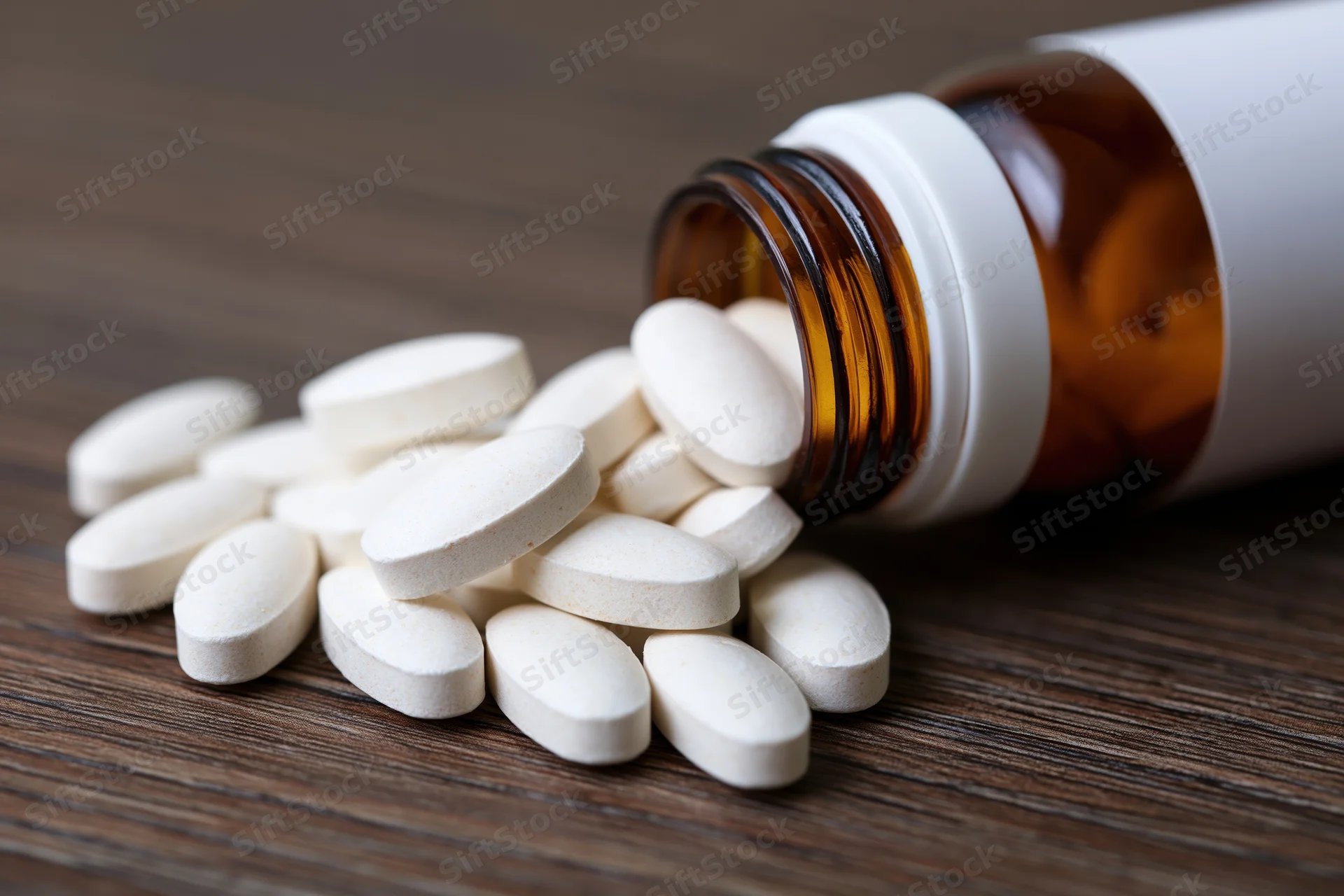 White oval supplement tablets spilling from an amber bottle onto a wooden surface