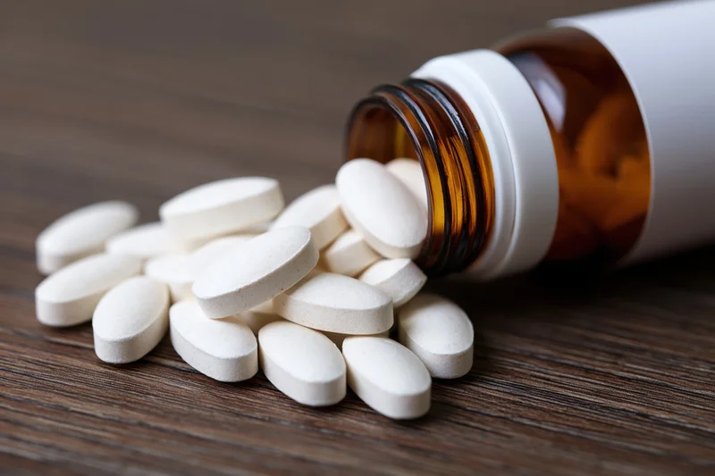 White oval supplement tablets spilling from an amber bottle onto a wooden surface