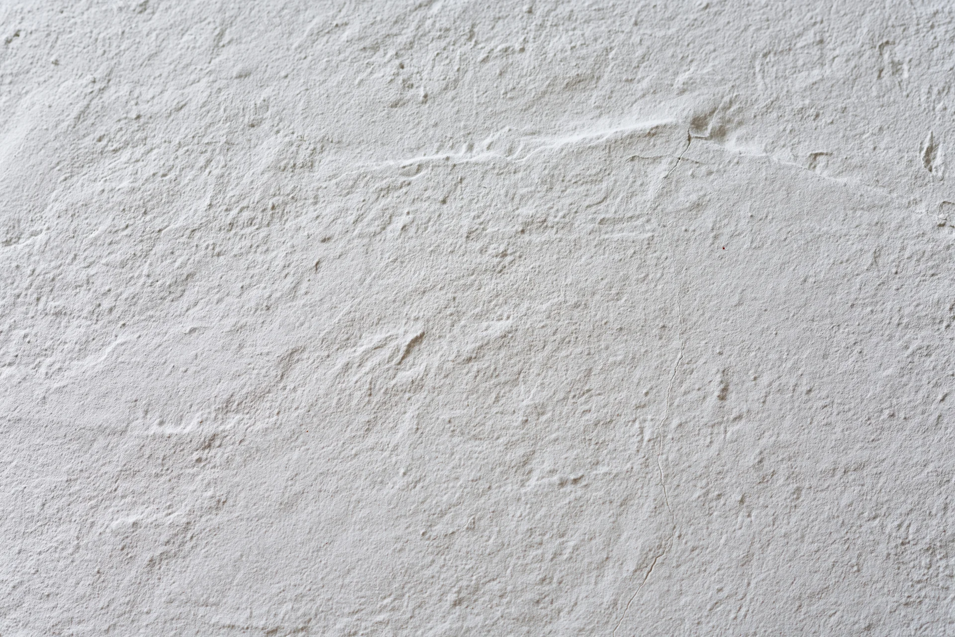 Close-up of a white plastered wall surface with rough texture and small cracks