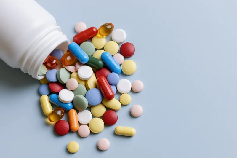 White plastic pill bottle lying on its side with assorted pills spilled onto a light blue surface