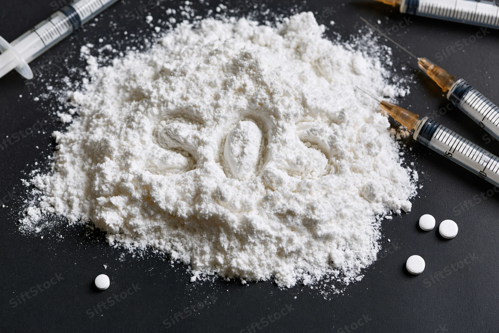 White powder with the letters SOS written in it surrounded by syringes and pills on a black surface