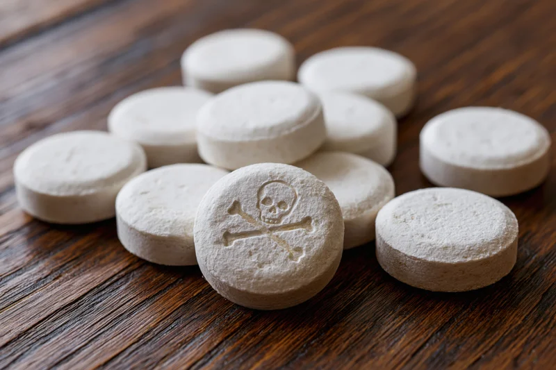 White pills scattered on dark wooden table one central pill