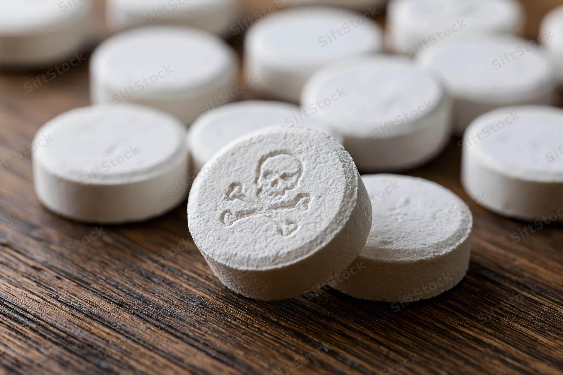 White round pills scattered on dark wooden table with skull and crossbones symbol in focus