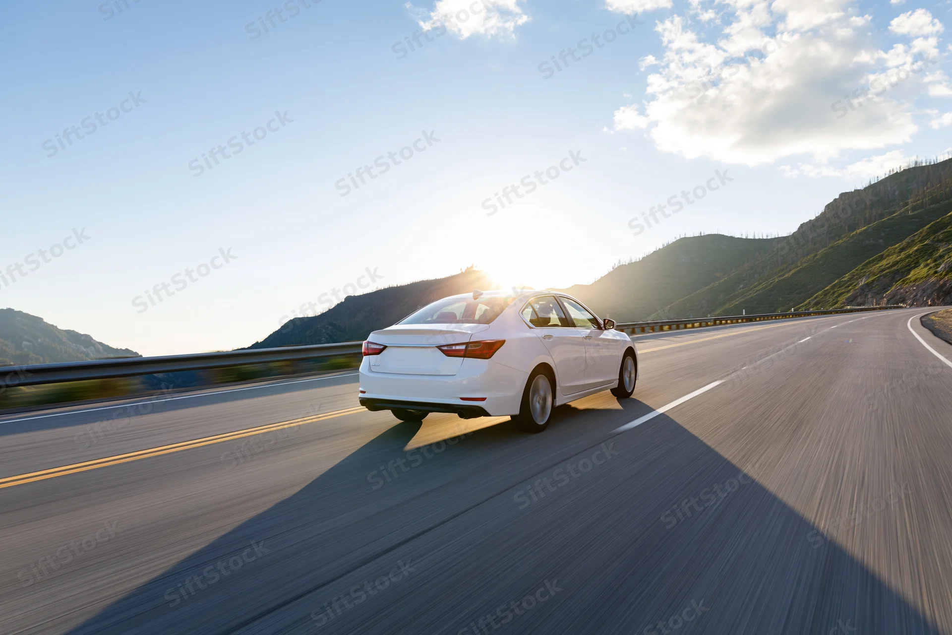 White sedan driving fast on a mountain highway at sunrise