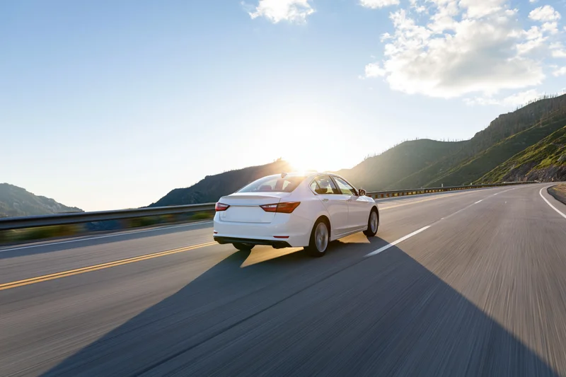 White sedan driving fast on a mountain highway at sunrise