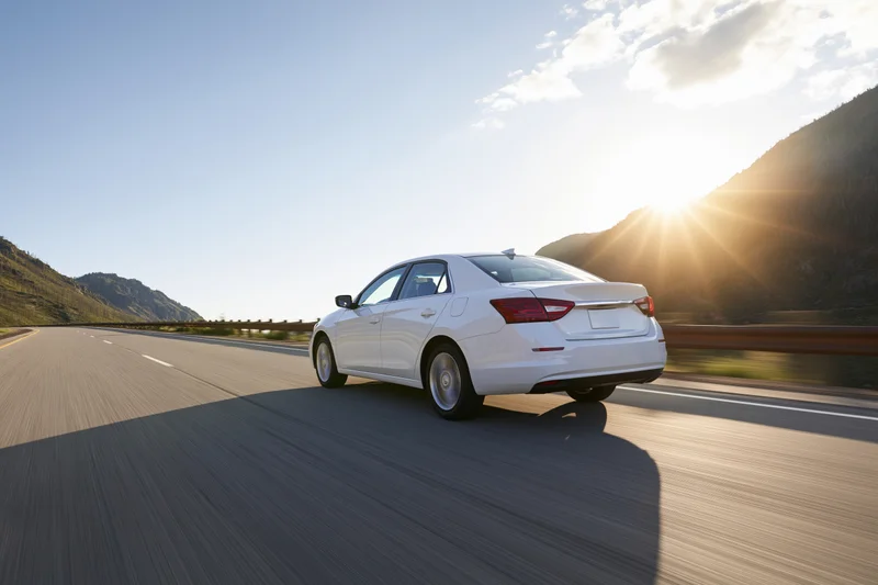 White sedan driving fast on a mountain highway at sunset