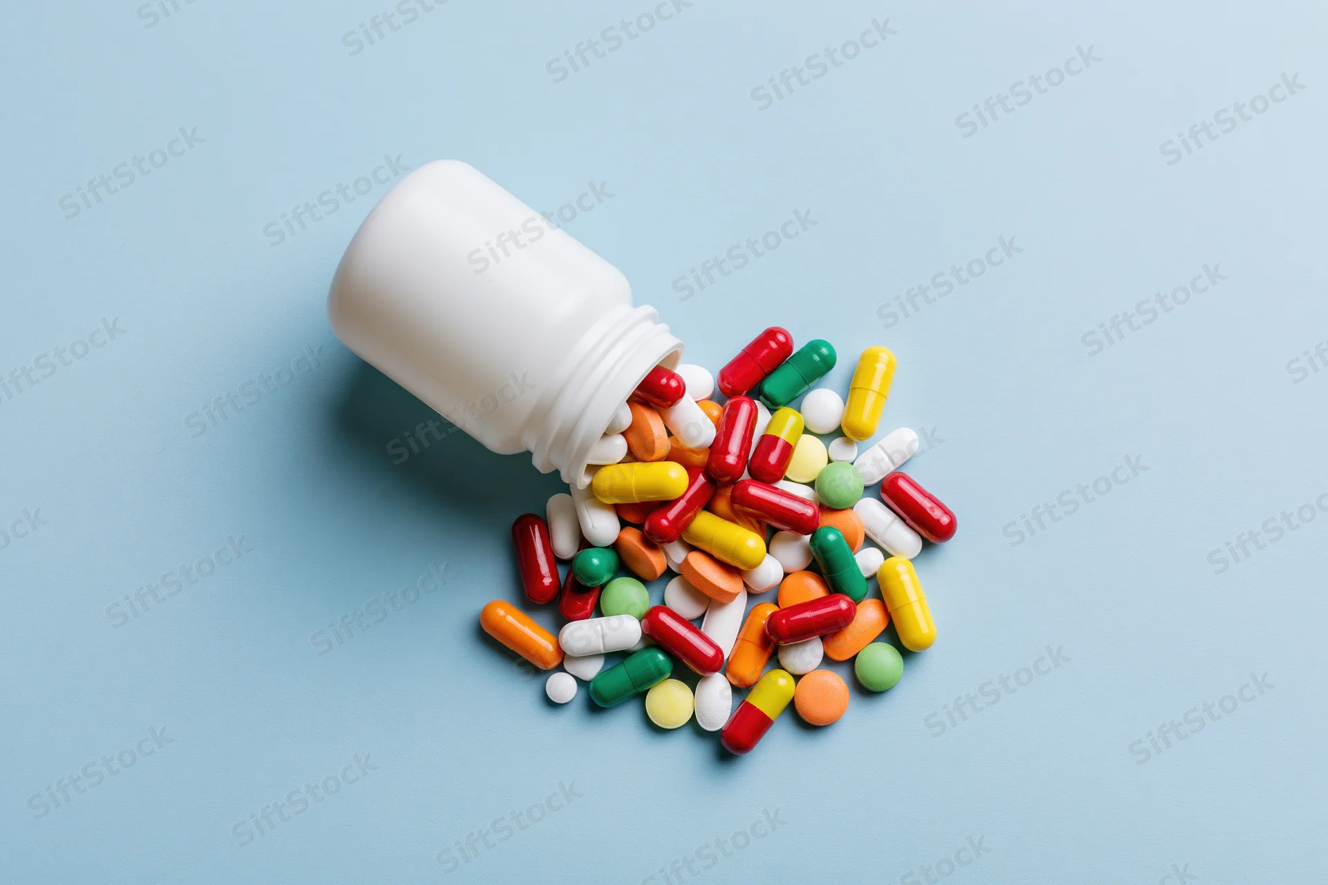 White pill bottle tipped over with colorful pills scattered on blue surface