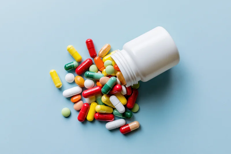 Colorful pills spilling from a white bottle on a light blue surface