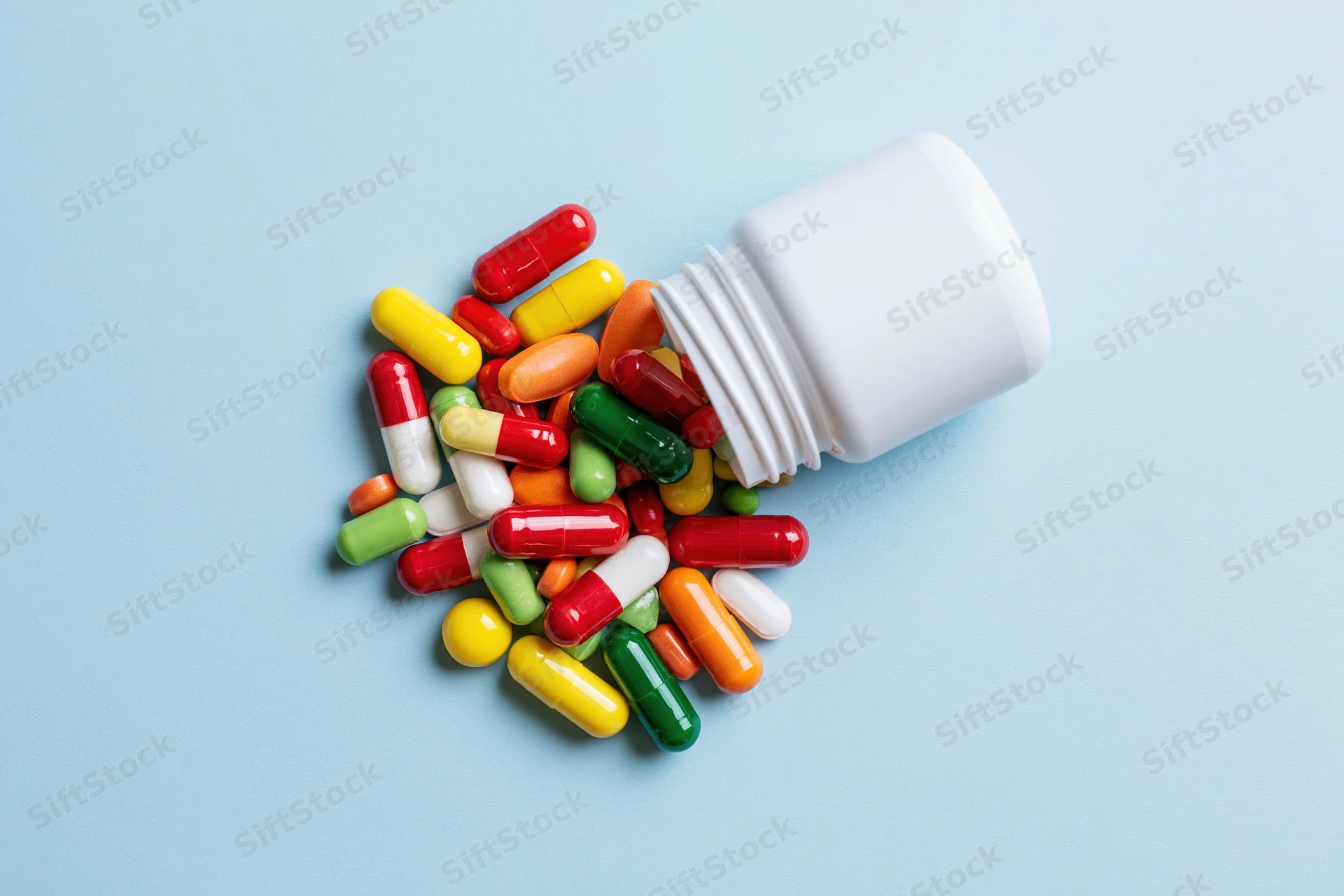 Colorful capsules spilling from a white pill bottle on a blue surface