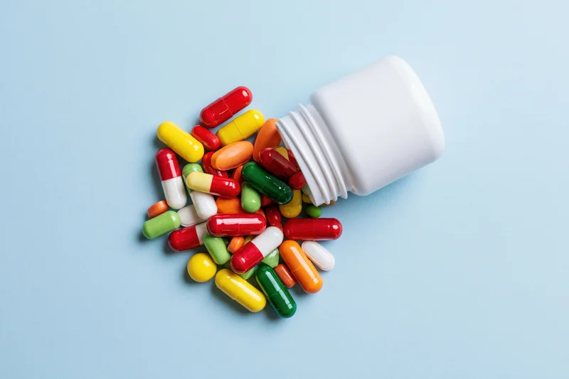 Colorful capsules spilling from a white pill bottle on a blue surface