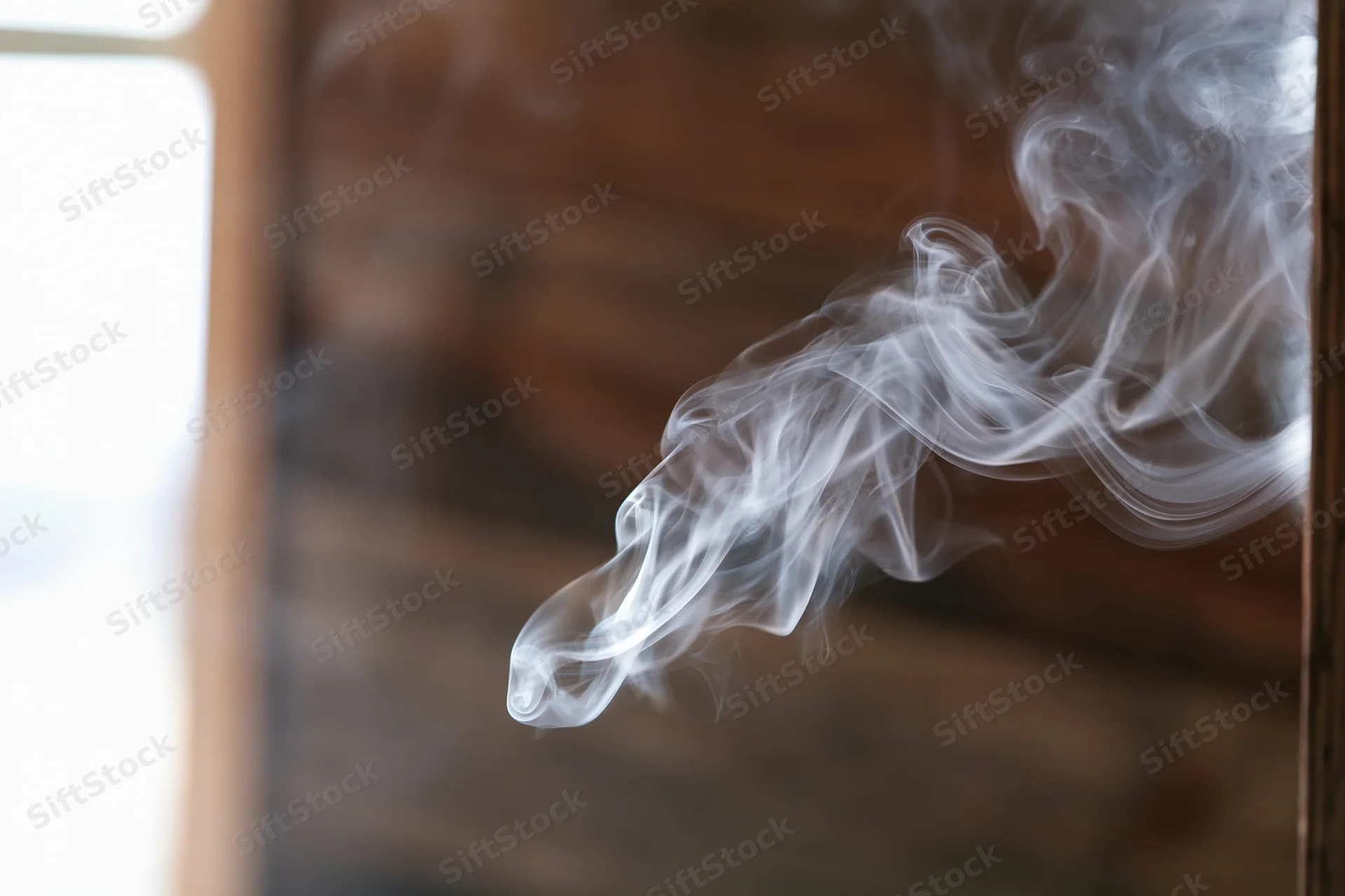 Wispy white smoke curling and dispersing in midair near a wooden wall interior