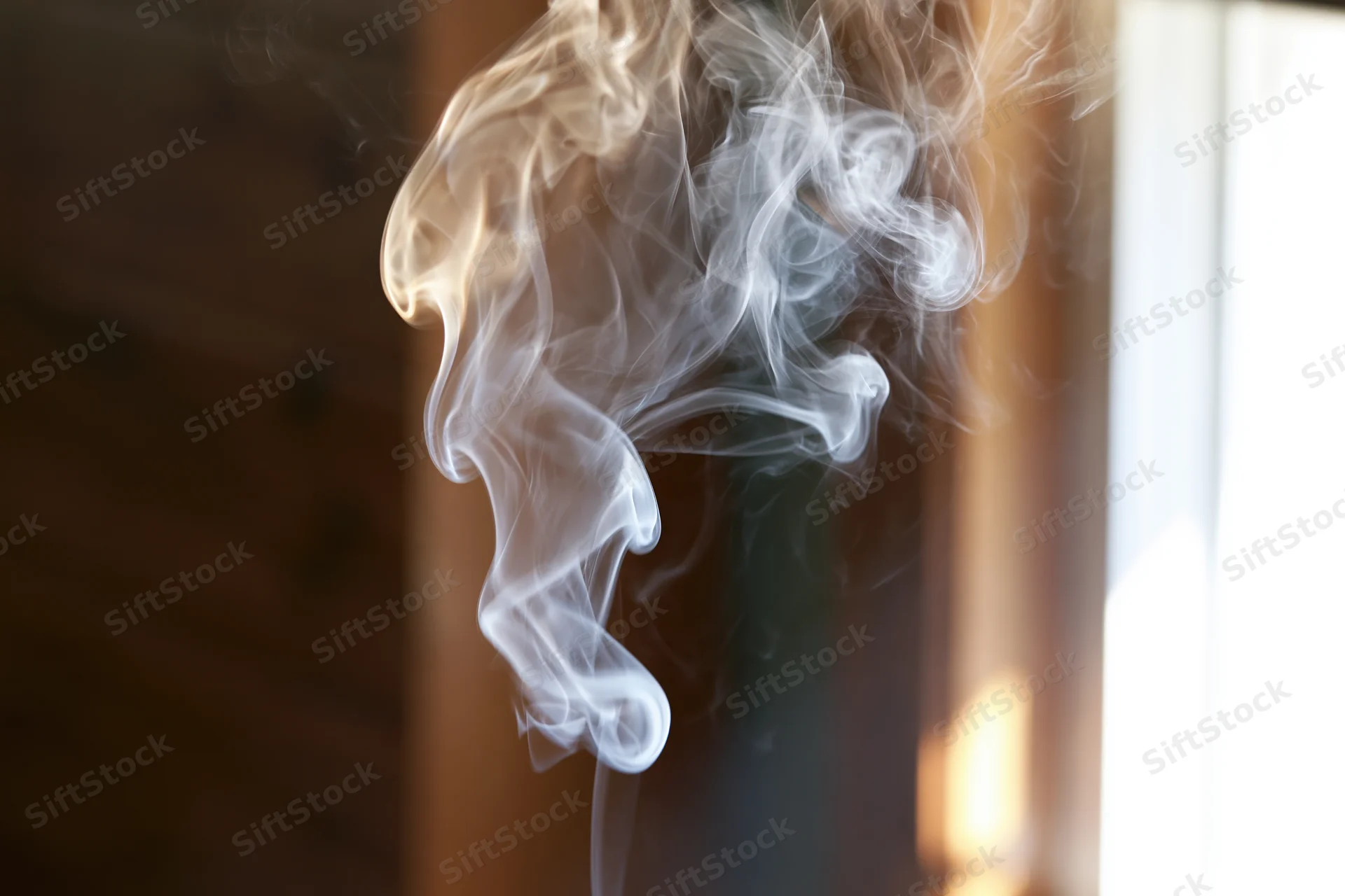Wispy white smoke curling and rising in a sunlit indoor space