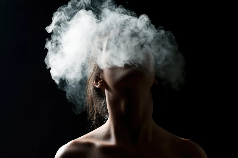 Woman exhaling smoke in silhouette against dark background