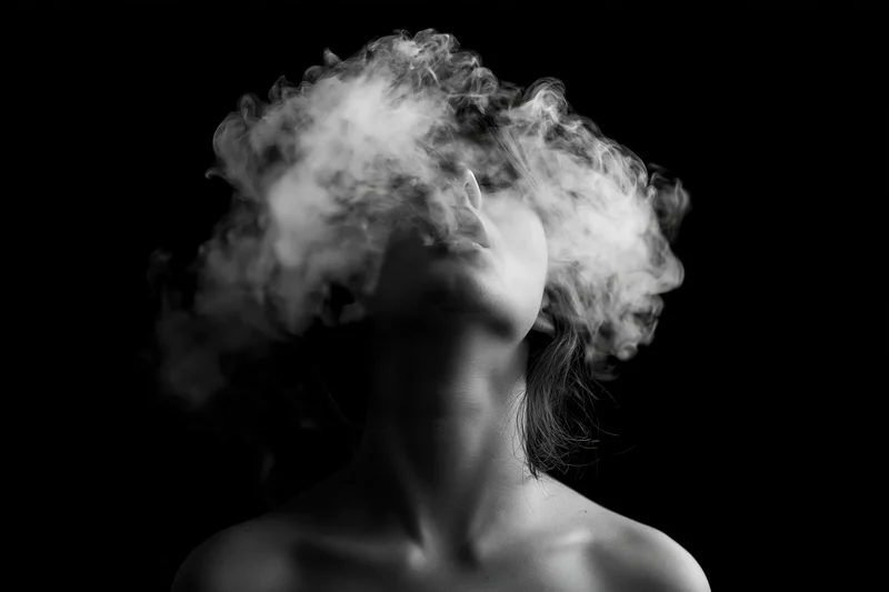 Woman exhaling smoke in silhouette against black background