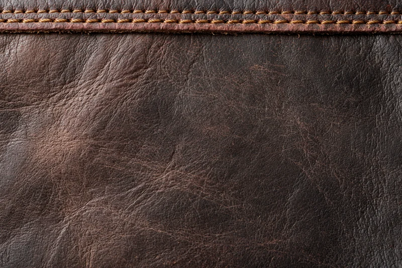Closeup of worn dark brown leather surface with visible stitching and grain texture