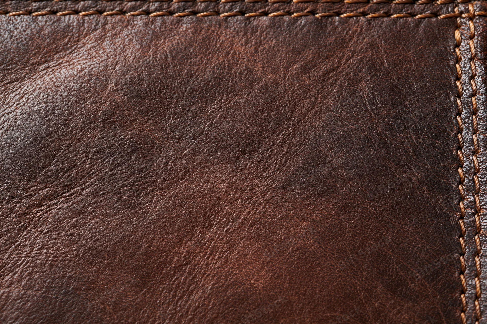 Closeup of worn dark brown leather surface with visible stitching and grain texture