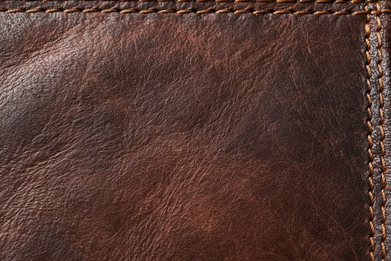 Closeup of worn dark brown leather surface with visible stitching and grain texture