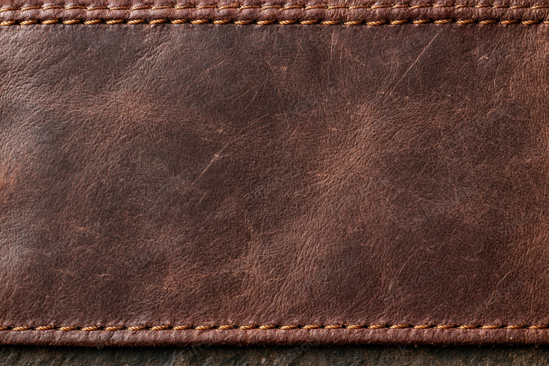 Closeup of worn dark brown leather surface with stitched edges