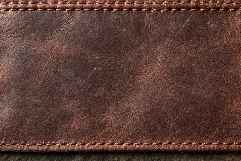 Closeup of worn dark brown leather surface with stitched edges
