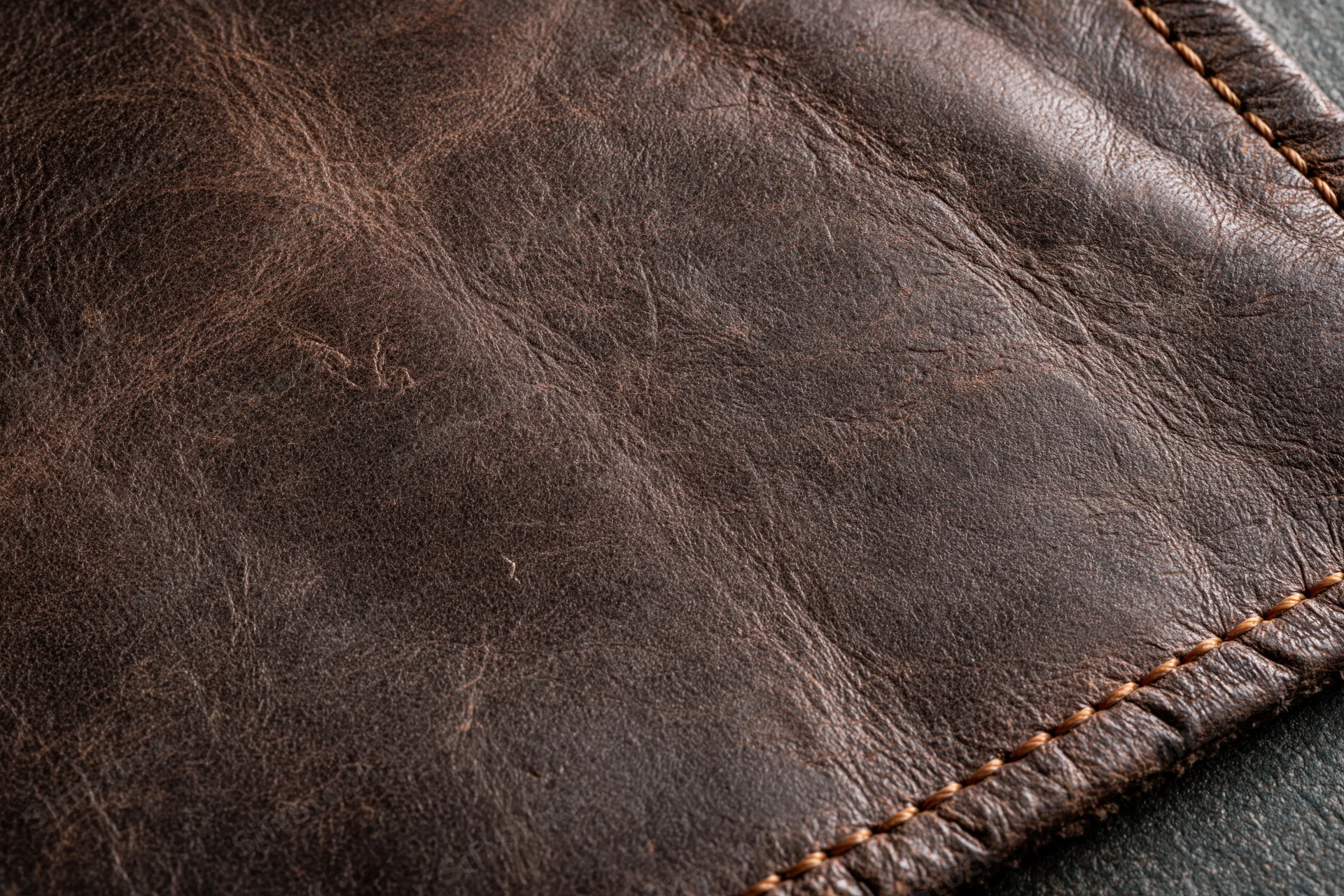 Closeup of worn dark brown leather surface with visible stitching and texture