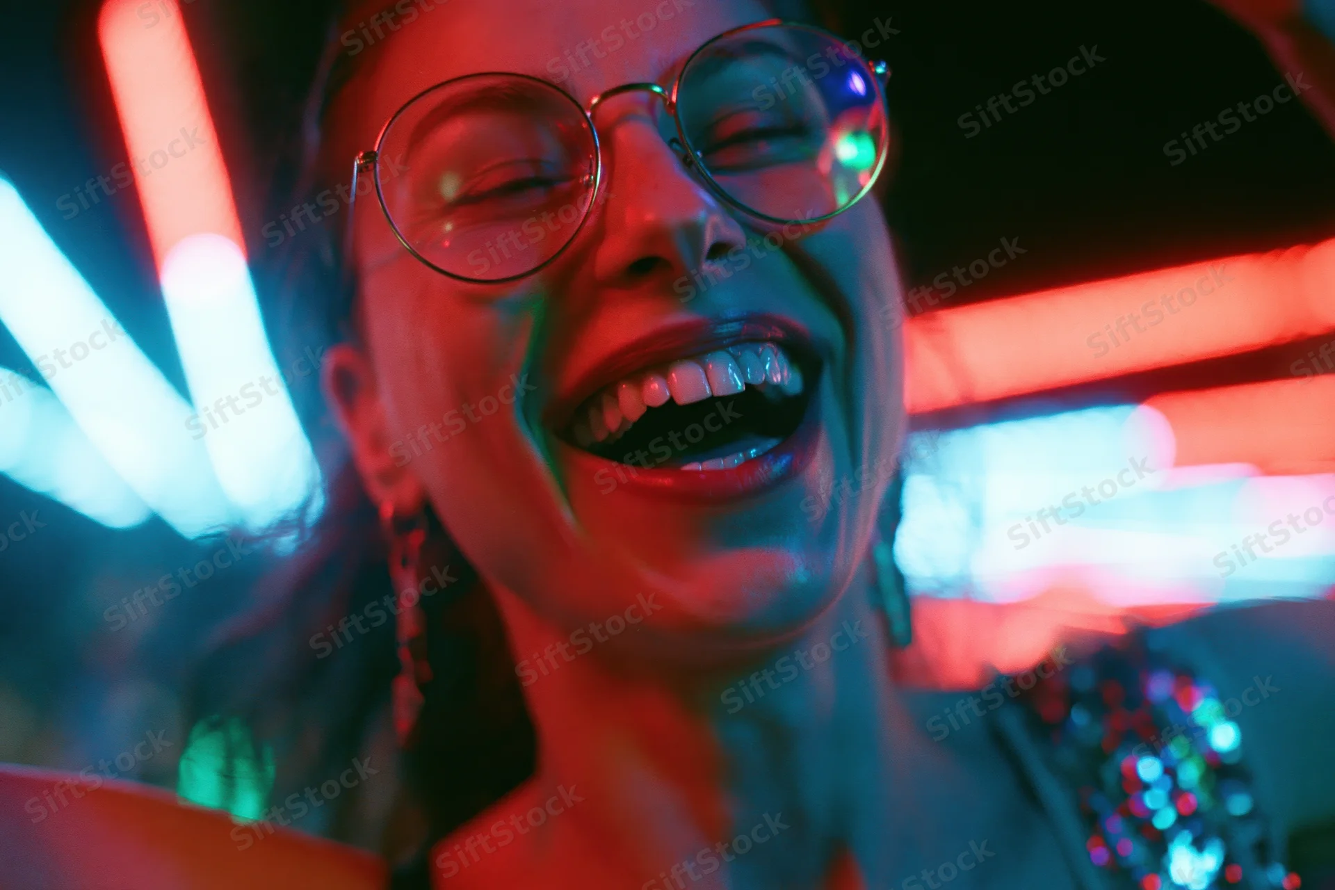 Young woman laughing with mouth open wearing round metal-framed glasses in a neon-lit club setting