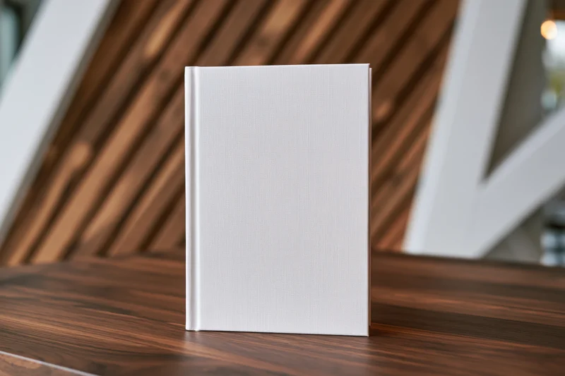 Blank white hardcover book standing upright on a dark walnut wooden table