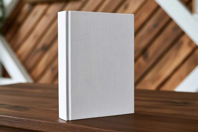 Blank white hardcover book standing upright on a dark walnut table
