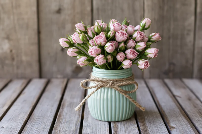 Pale pink rose buds in a ribbed mint vase tied with twine on a wooden table