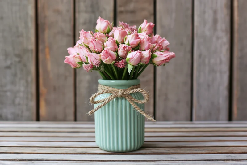 Pale pink rose buds in a ribbed mint ceramic vase tied with twine on a wooden table