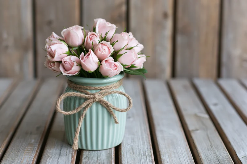 Pale pink rose buds in a ribbed mint vase tied with twine on a weathered wooden table