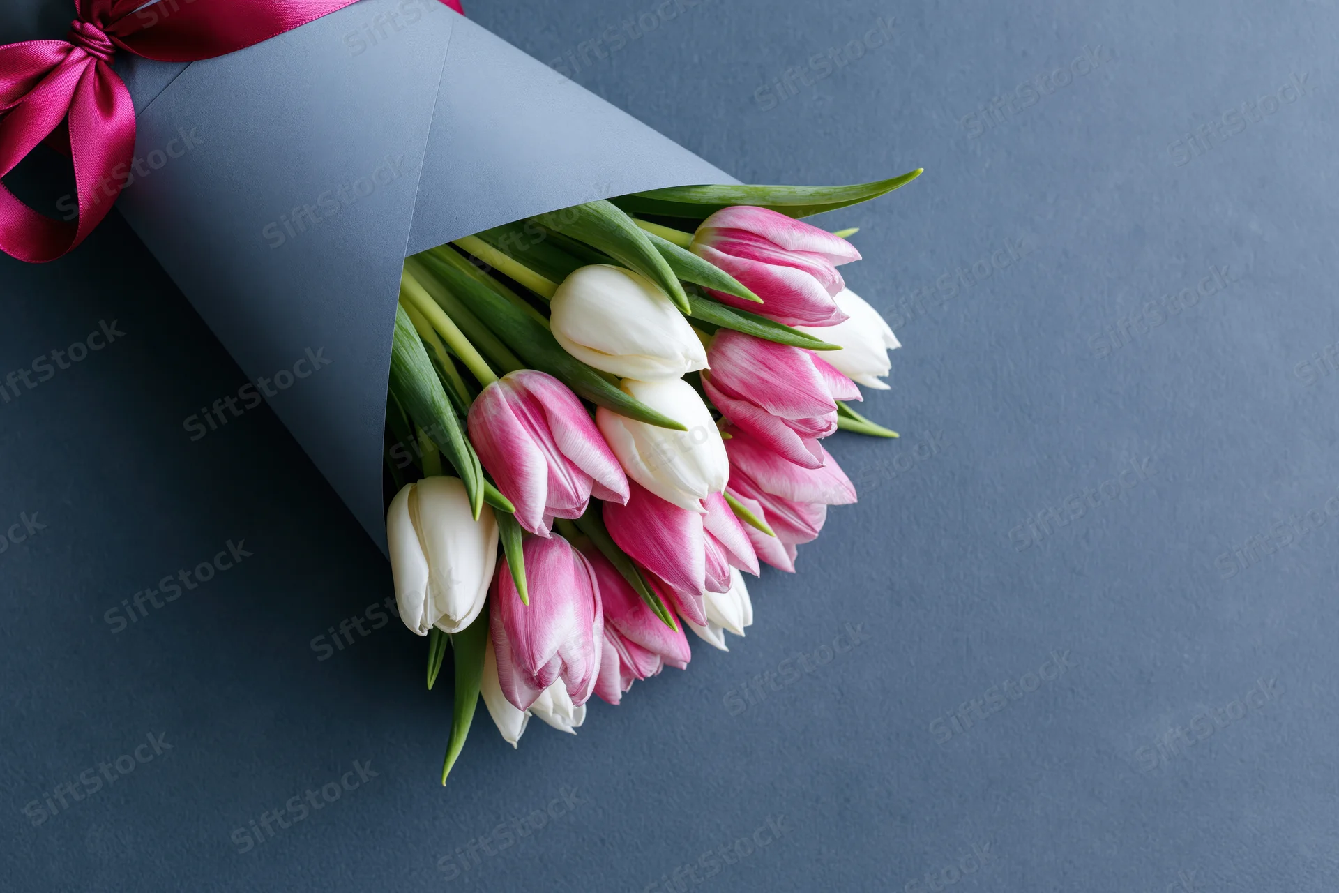 Bouquet of pink and white tulips wrapped in grey matte paper with pink ribbon on dark surface